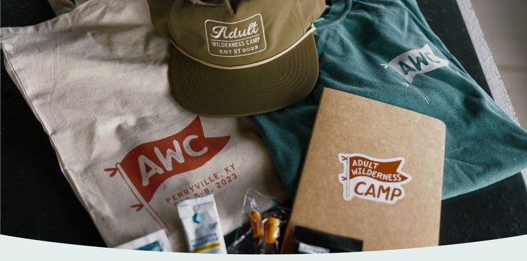 Collection of AWC branded items including a cap, t-shirt, and notebook on a table.